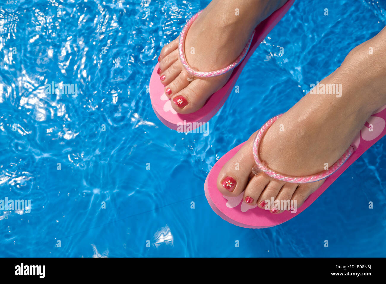 Feet wearing flip-flops dangling over the side of a paddling pool Stock Photo