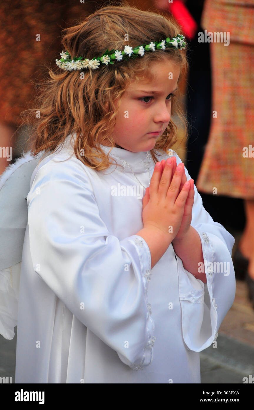 Little blond girl dressed as an angel in white with wings, flower garland and hands clasped in prayer during the Semana Santa,  Stock Photo