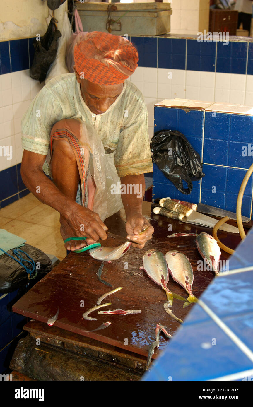 Man wearing an orange turban using his foot to hold the fish he is cleaning at the Muttrah fish market, Muscat, Sultanate of Om Stock Photo