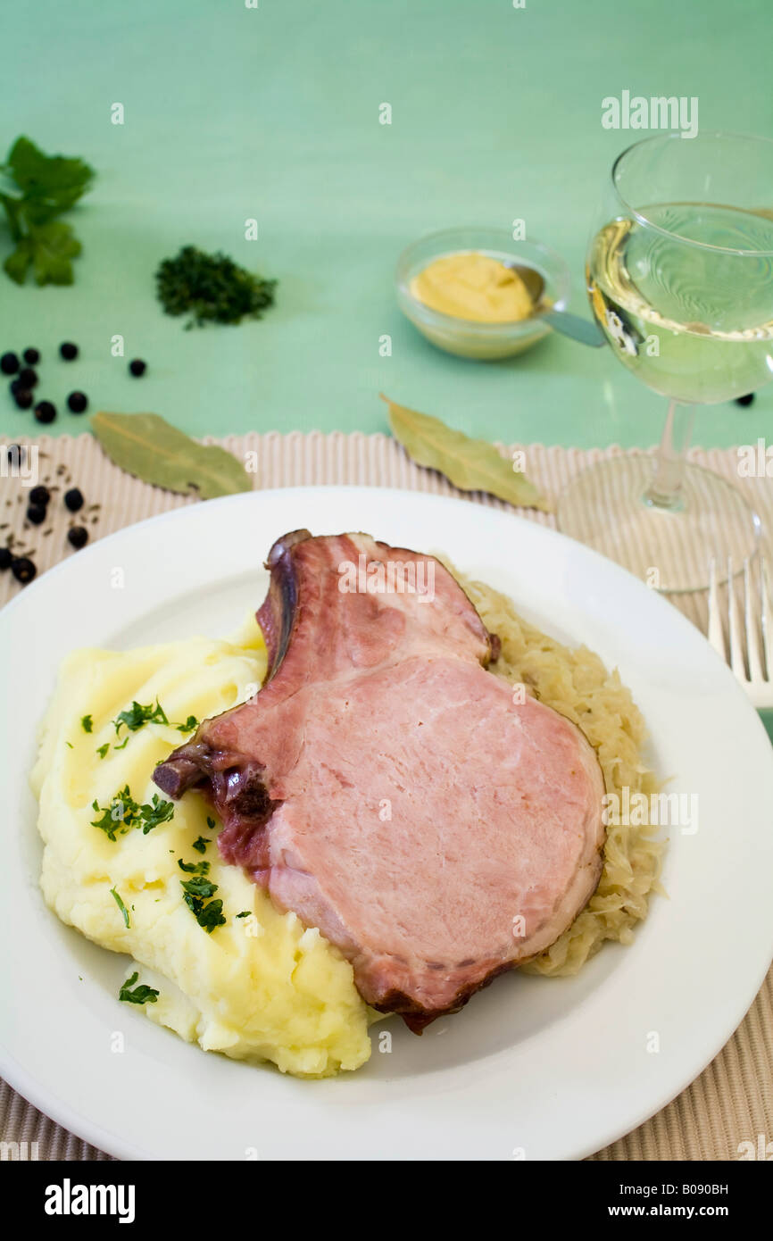 Smoked pork loin with sauerkraut, mashed potatoes and spices served with a glass of white wine Stock Photo