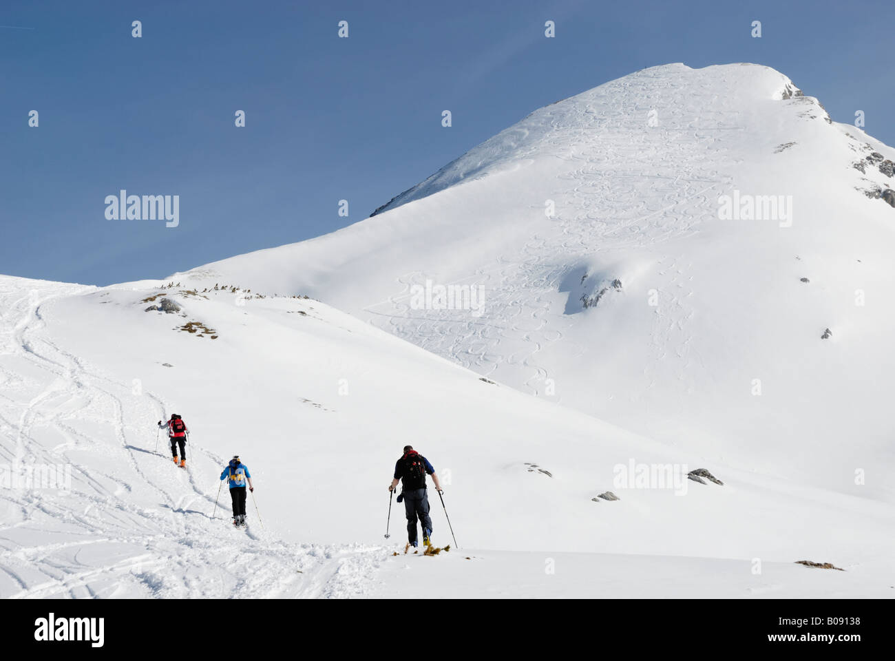 Mountaineers on touring skis crossing a snowy slope leading up to a snow-covered mountain peak laced with ski tracks, Rofan Ran Stock Photo