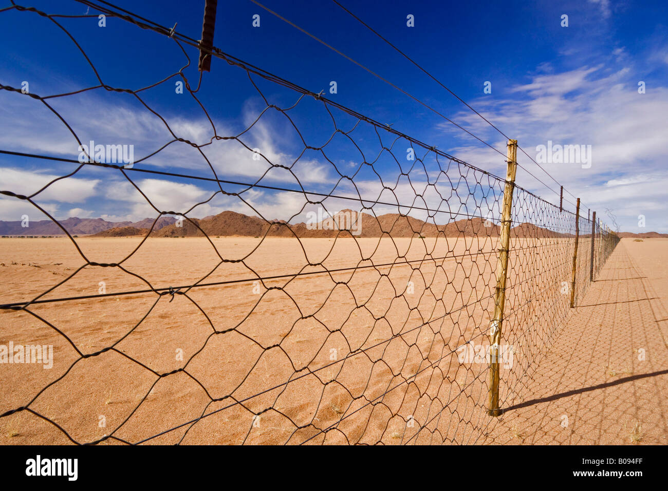 Dead straight farmer's wire fence, chain-link fencing over flat desert sand on the edge of the Namib Desert, Namibia, Africa Stock Photo