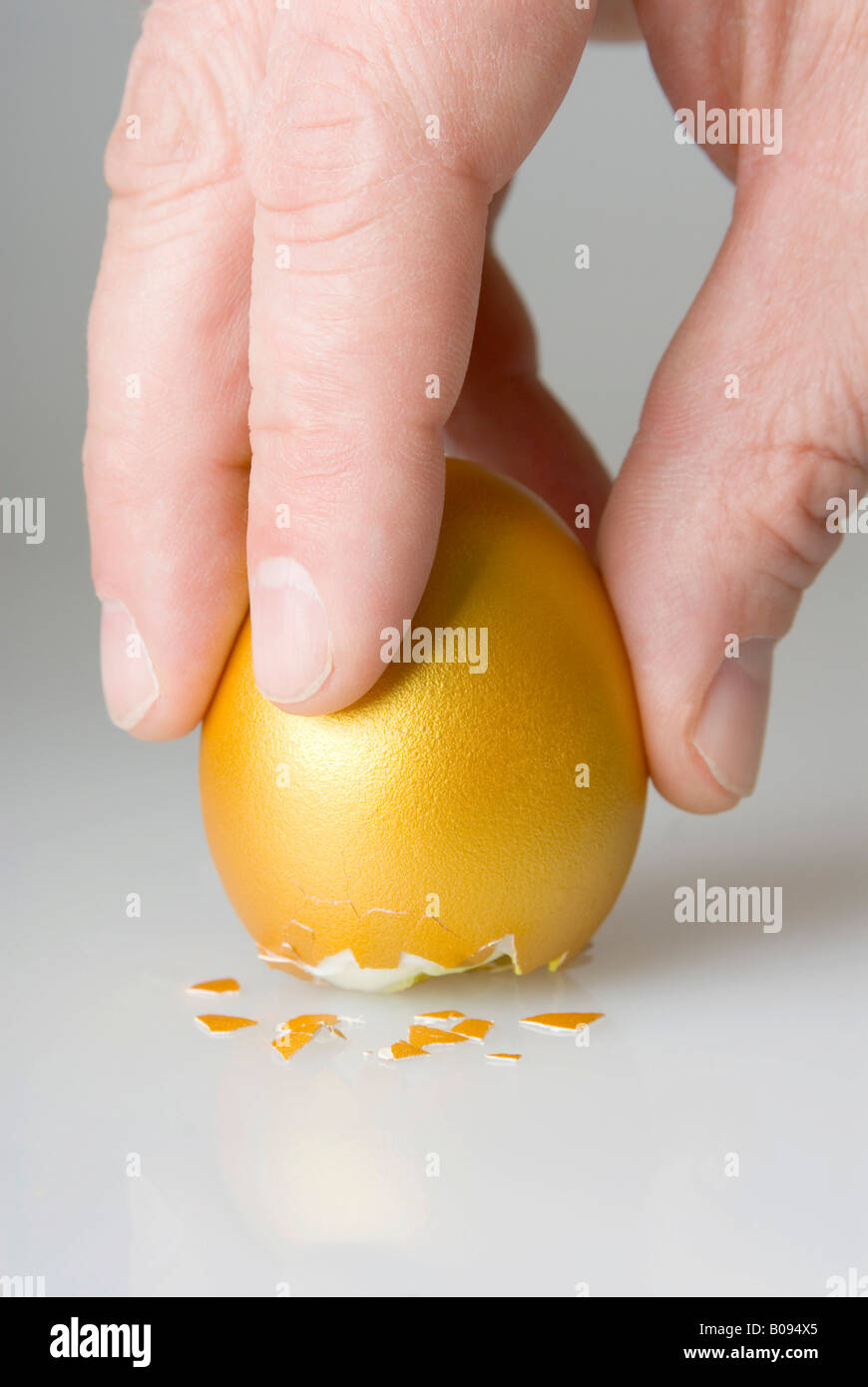 Egg of Columbus, hand positioning golden egg on its cracked bottom Stock Photo