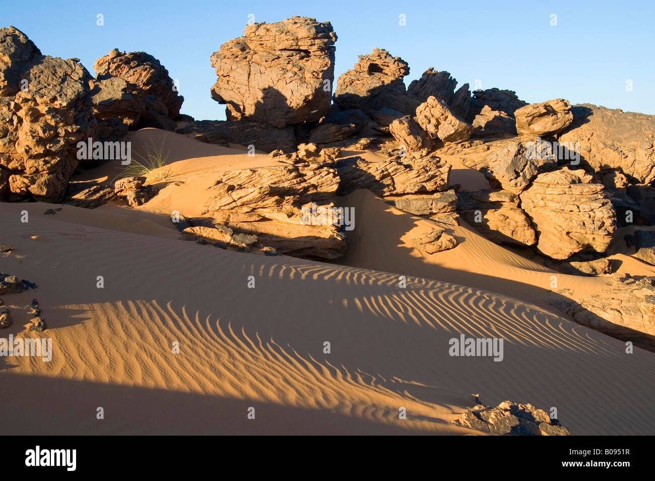 Eroded rock formation above sand dunes, ripples, evening sun, Acacus Mountains, Libya, North Africa Stock Photo