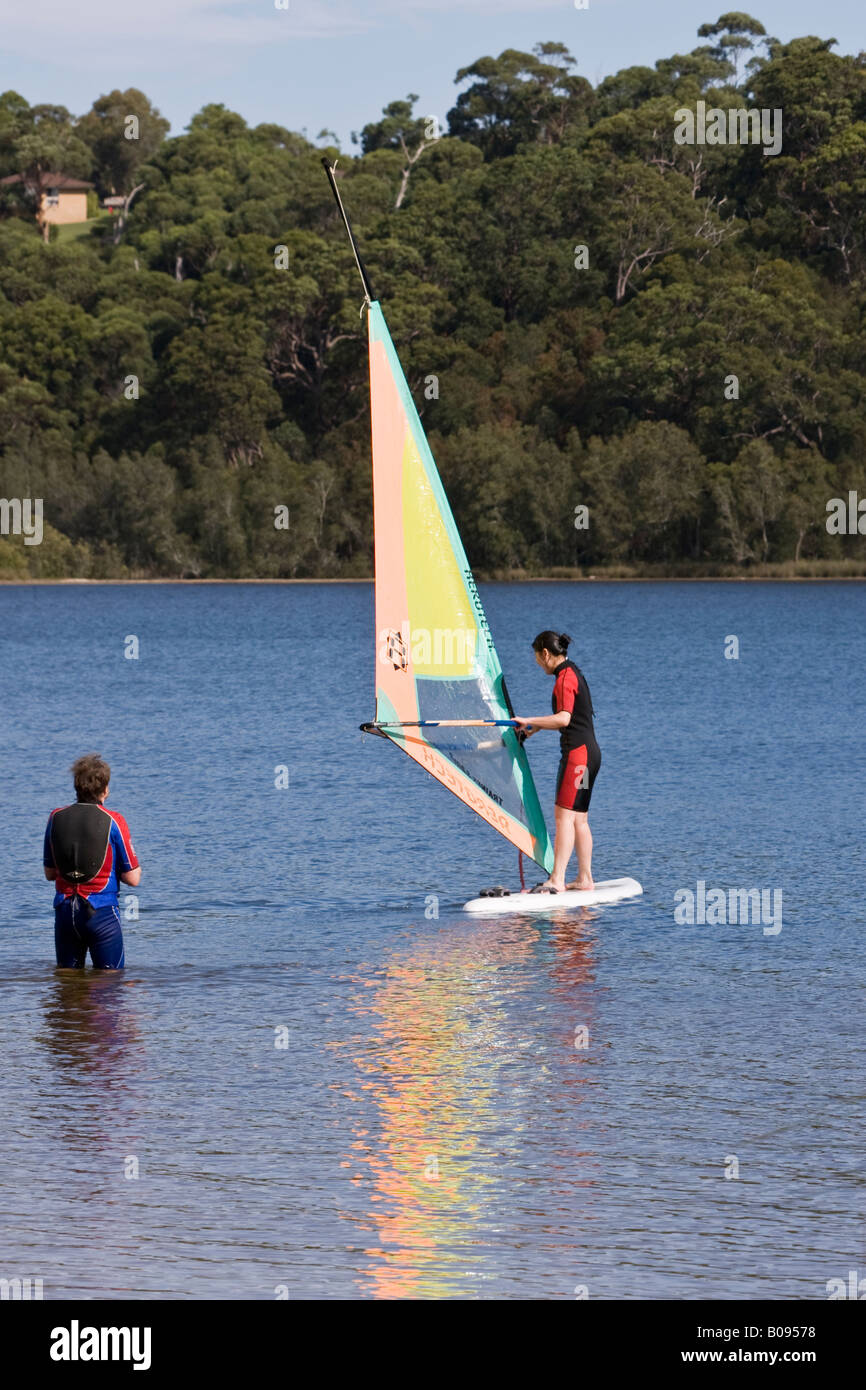 A boy teaching his girlfriend to windsurf on Narrabeen Lakes in NSW