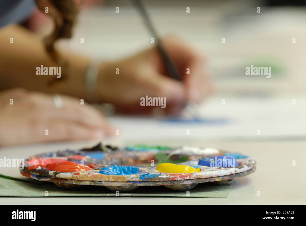 Close up of artist's paint pallette with hands painting in background Stock Photo