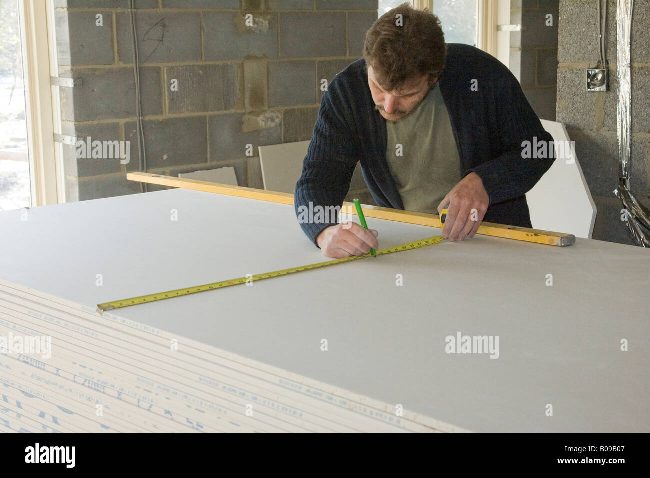 Builder Worker Measuring And Cutting Plasterboard Stock