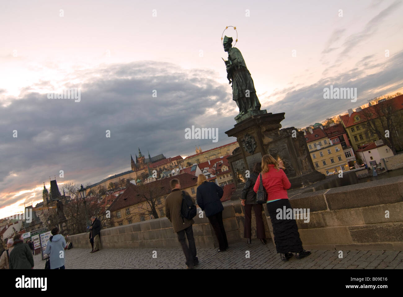 Horizontal wide angle of the St John of Nepomuk statue on the Charles Bridge being touched for good luck by tourists at sunset. Stock Photo