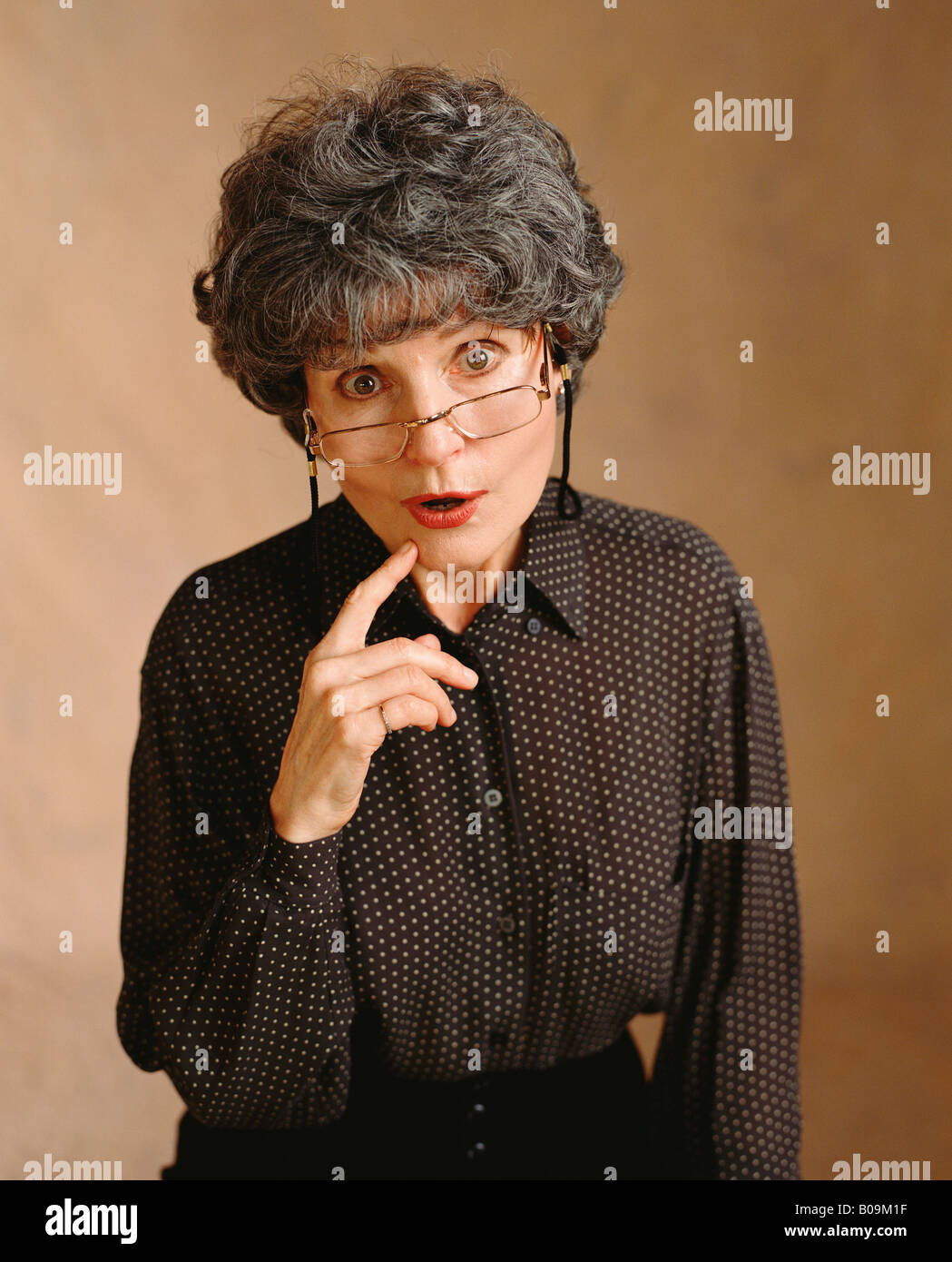 An expression of humor from an older woman with gray hair and reading glasses in a studio portrait. Stock Photo