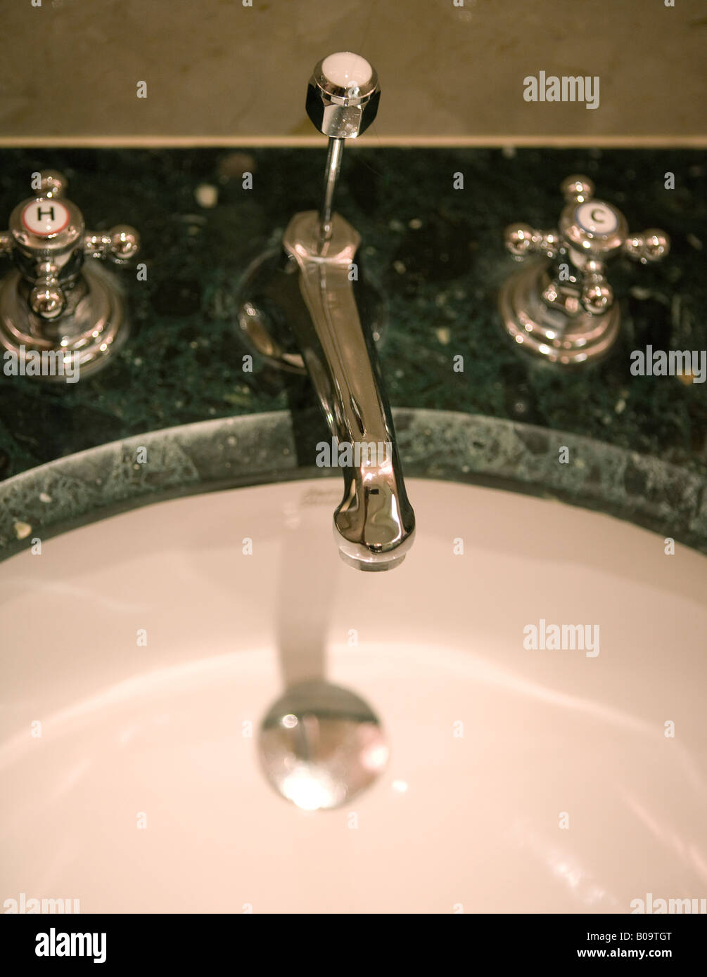 Silver, old-fashioned watertap with separate hot and cold taps, green marble and white sink Stock Photo