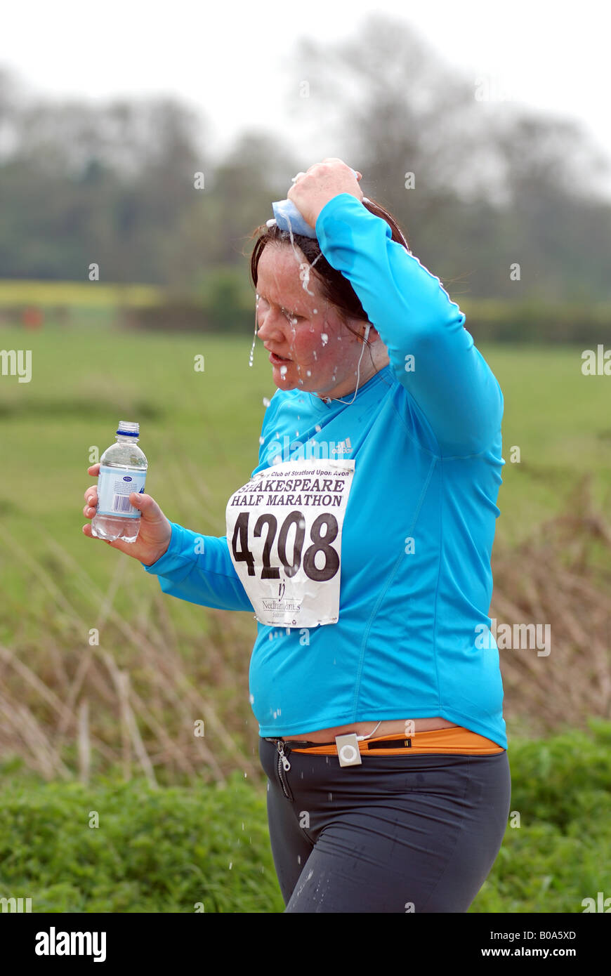 Woman runner in half marathon race sponging head and carrying water