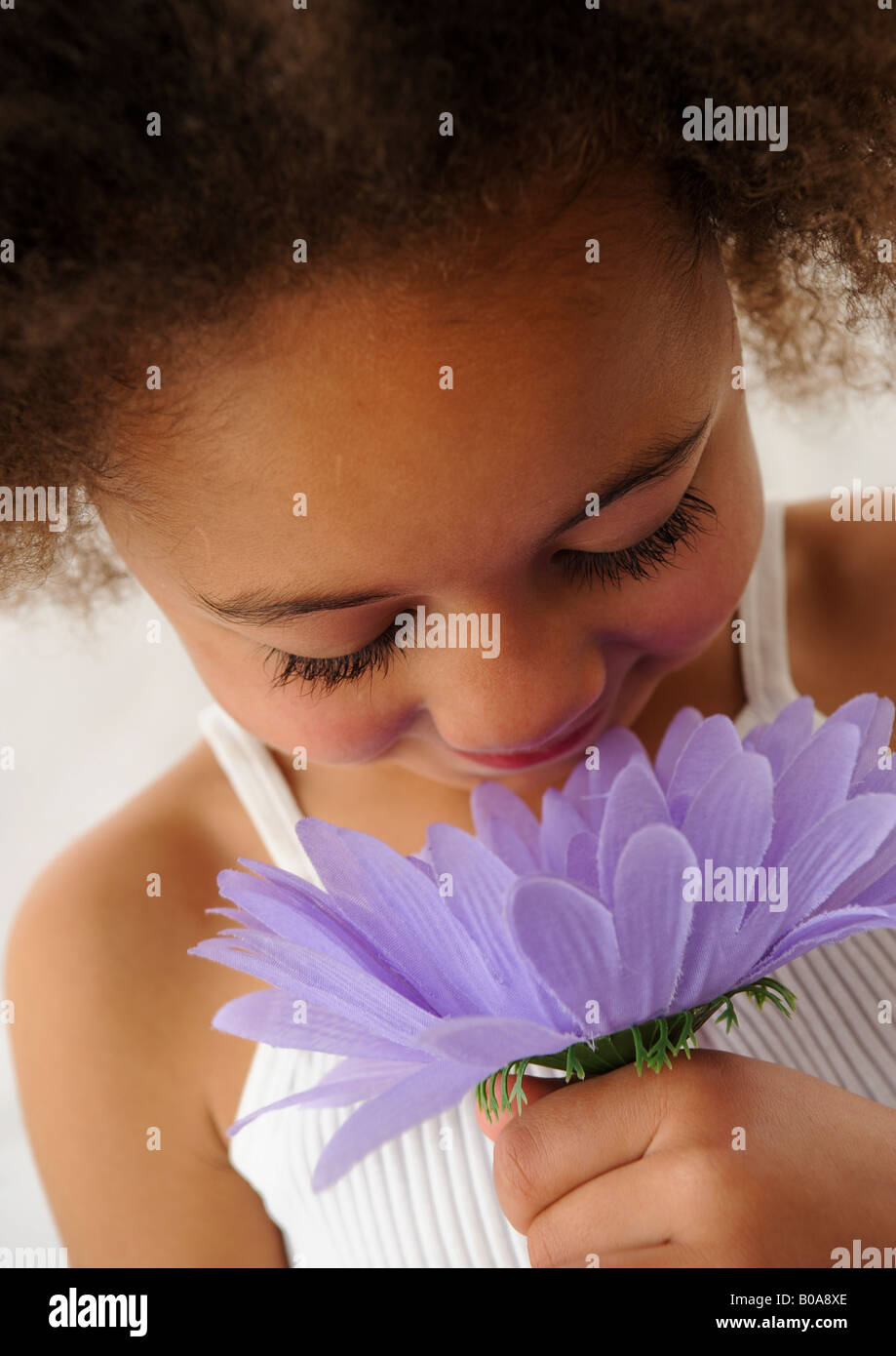Closeup of a cutie girl in white slipover with Afro hairstyle appreciating  sweet scented fragrance in artificial gerbera flower Stock Photo - Alamy