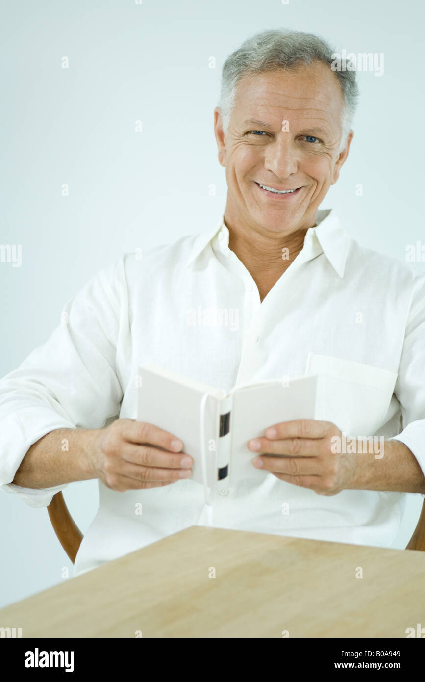 Mature man sitting, holding book, smiling at camera Stock Photo