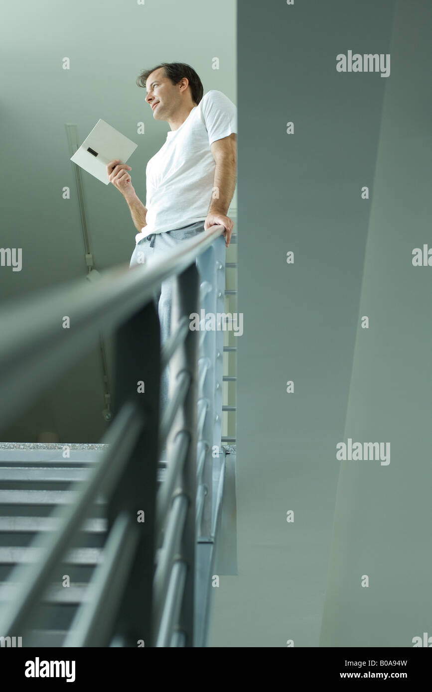 Man standing at top of staircase, holding book, looking away Stock Photo