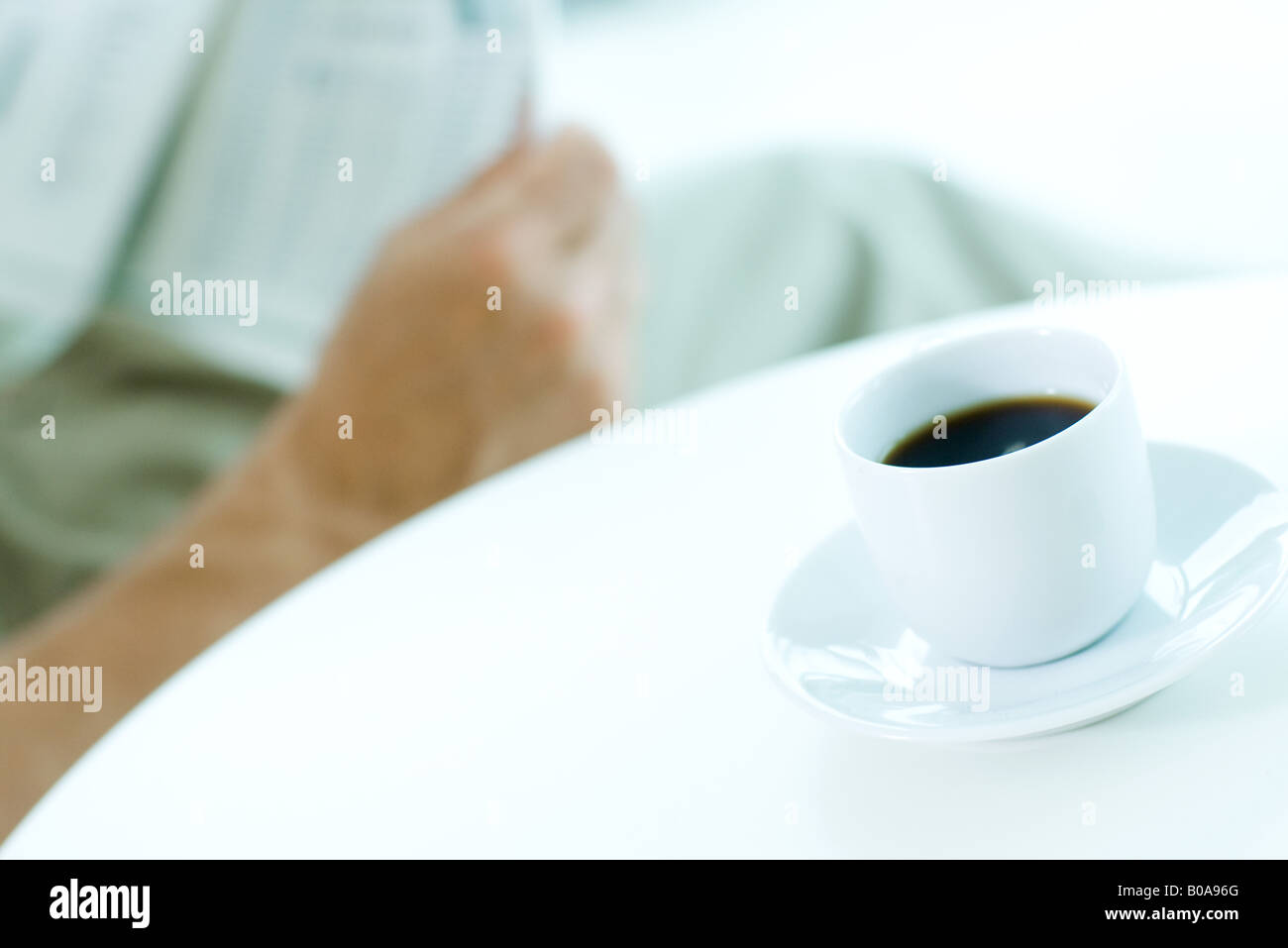 Man reading newspaper, focus on coffee cup in foreground Stock Photo