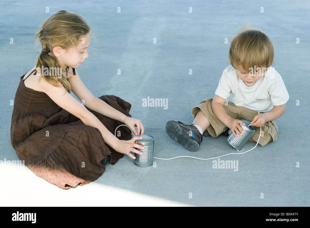Brother and sister sitting on the ground, playing with tin can phone Stock Photo