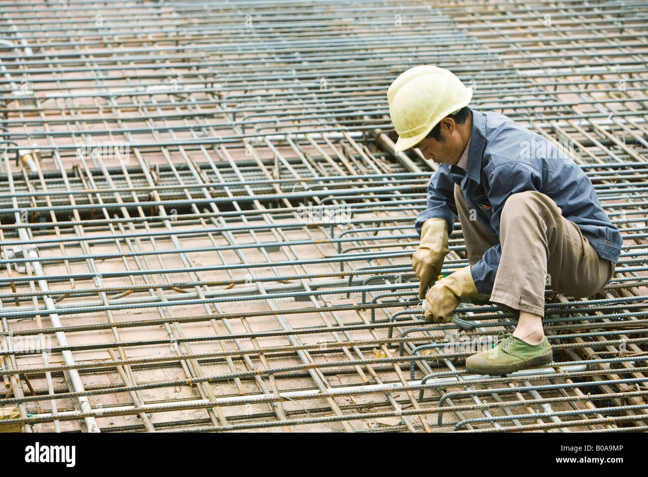 Man crouching at construction site, building steel framework Stock