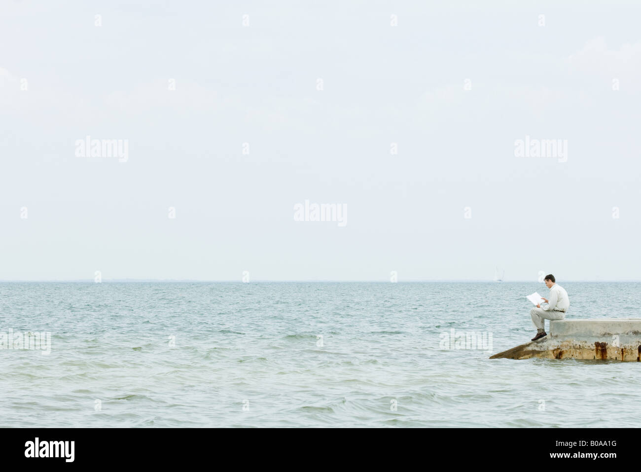 Man sitting at the end of pier, reading book, in the distance Stock Photo
