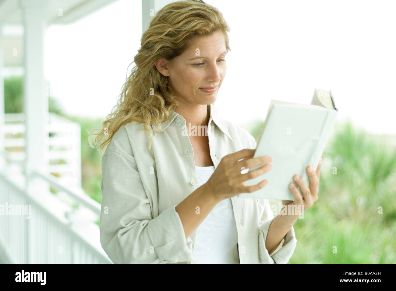 Woman standing on porch, reading book, close-up Stock Photo