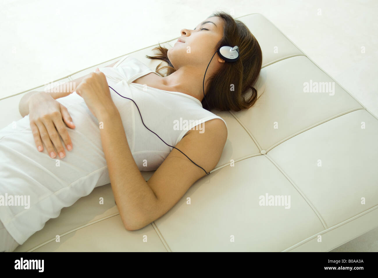 Woman lying on back, listening to headphones, eyes closed Stock Photo
