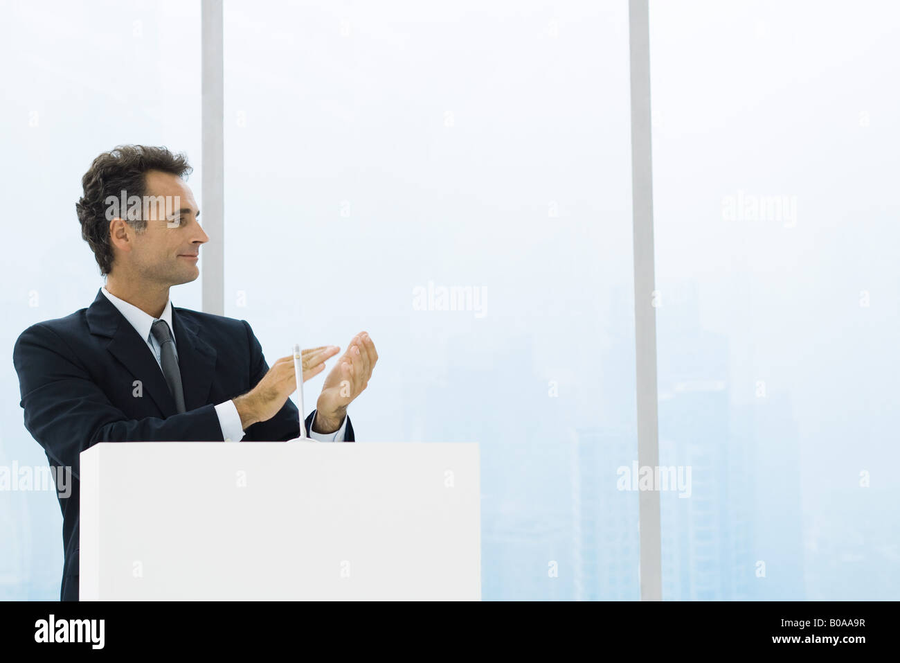 Businessman at lectern clapping hands, looking away, smiling Stock Photo