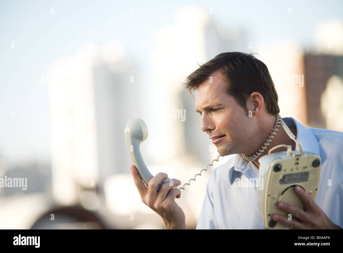 Man wrapping landline phone cord around neck, looking at receiver Stock Photo