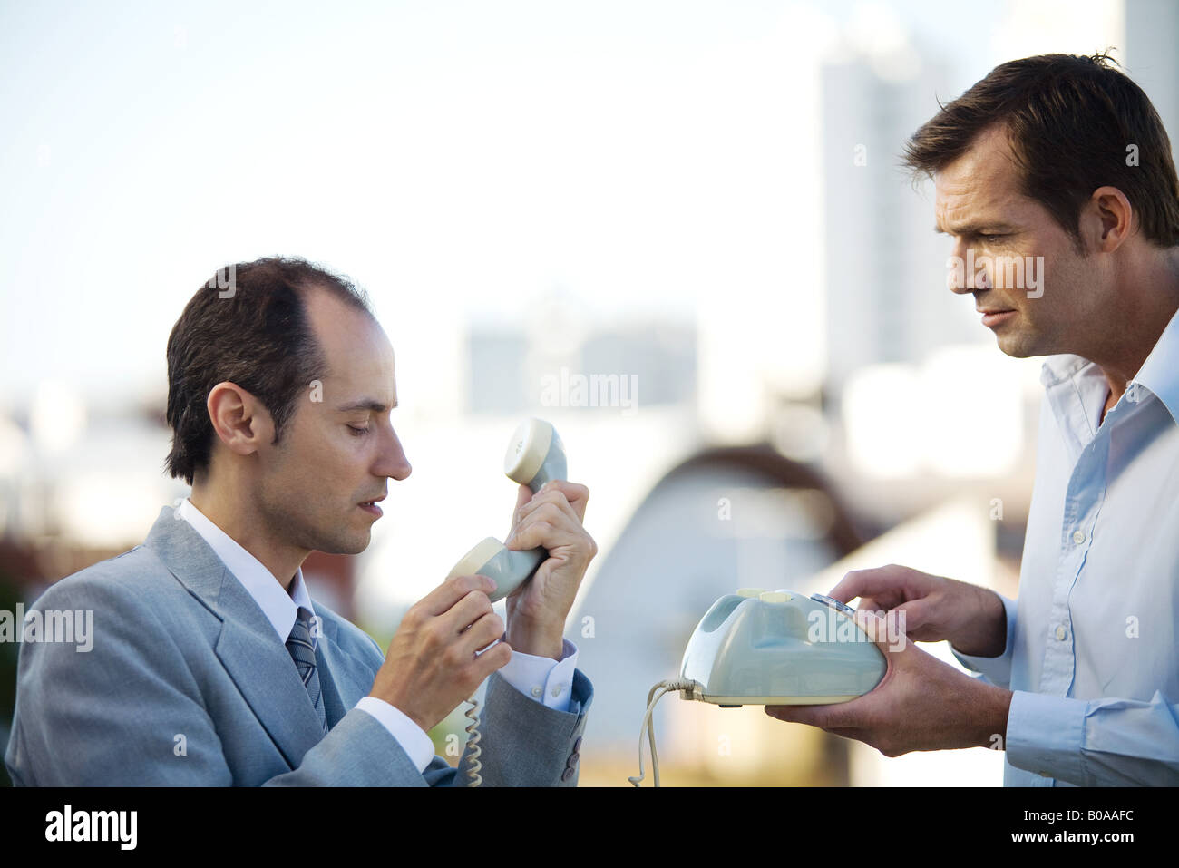 Two businessmen standing face to face, looking at landline phone, side view Stock Photo