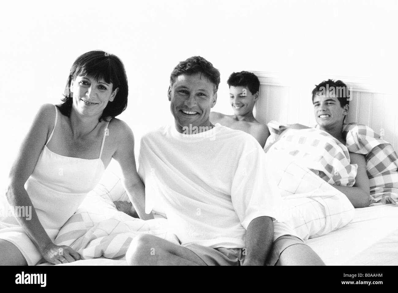 Family sitting on bed together, man and woman smiling at camera Stock Photo