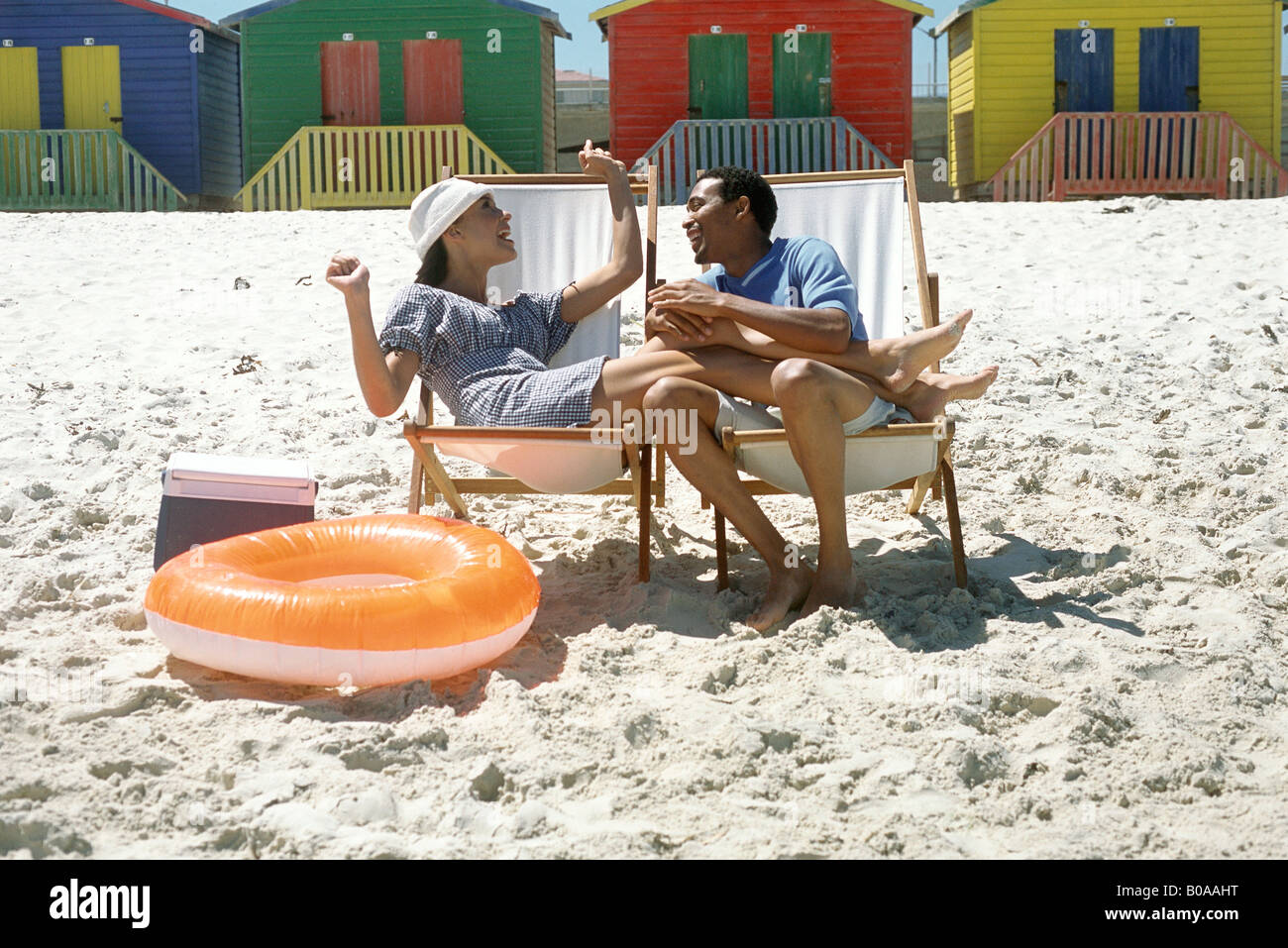 Couple sitting in lounge chairs at the beach, smiling, woman's legs on man's lap Stock Photo