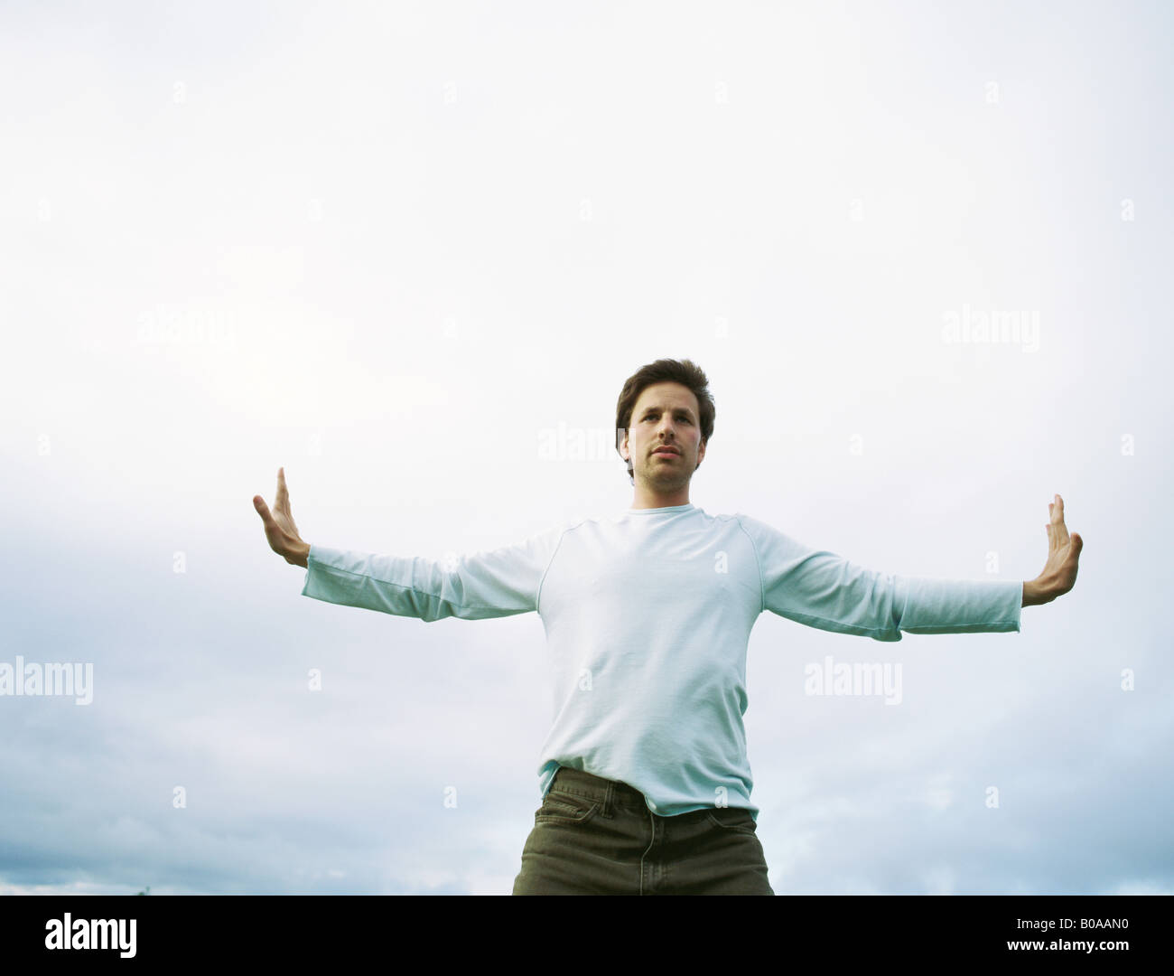 Man standing outdoors with arms outstretched, low angle view Stock Photo