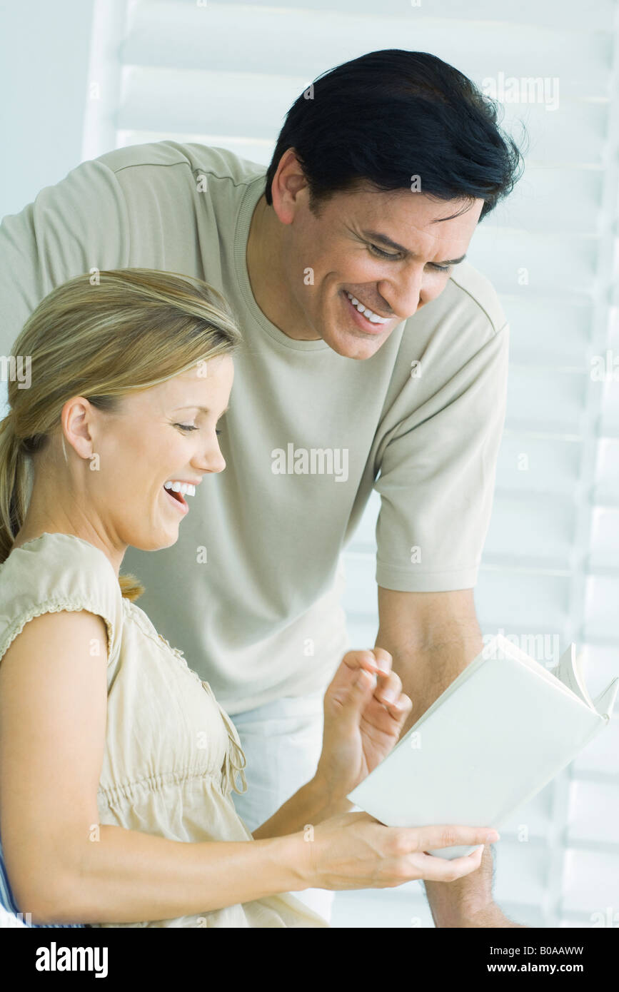Couple reading book together, man looking over woman's shoulder, both smiling Stock Photo