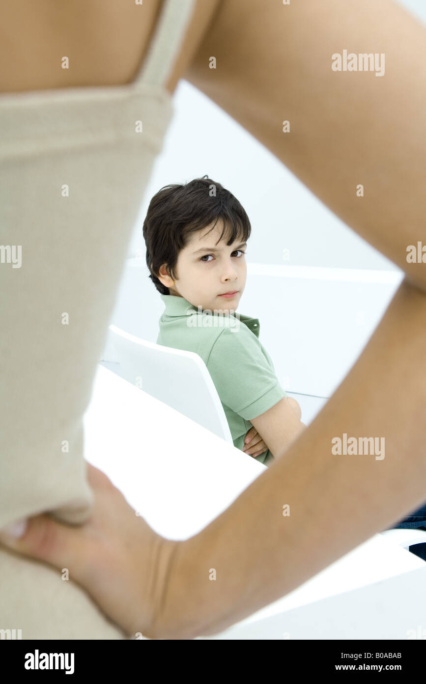 Boy sulking, looking over shoulder at mother in foreground with hand on hip Stock Photo