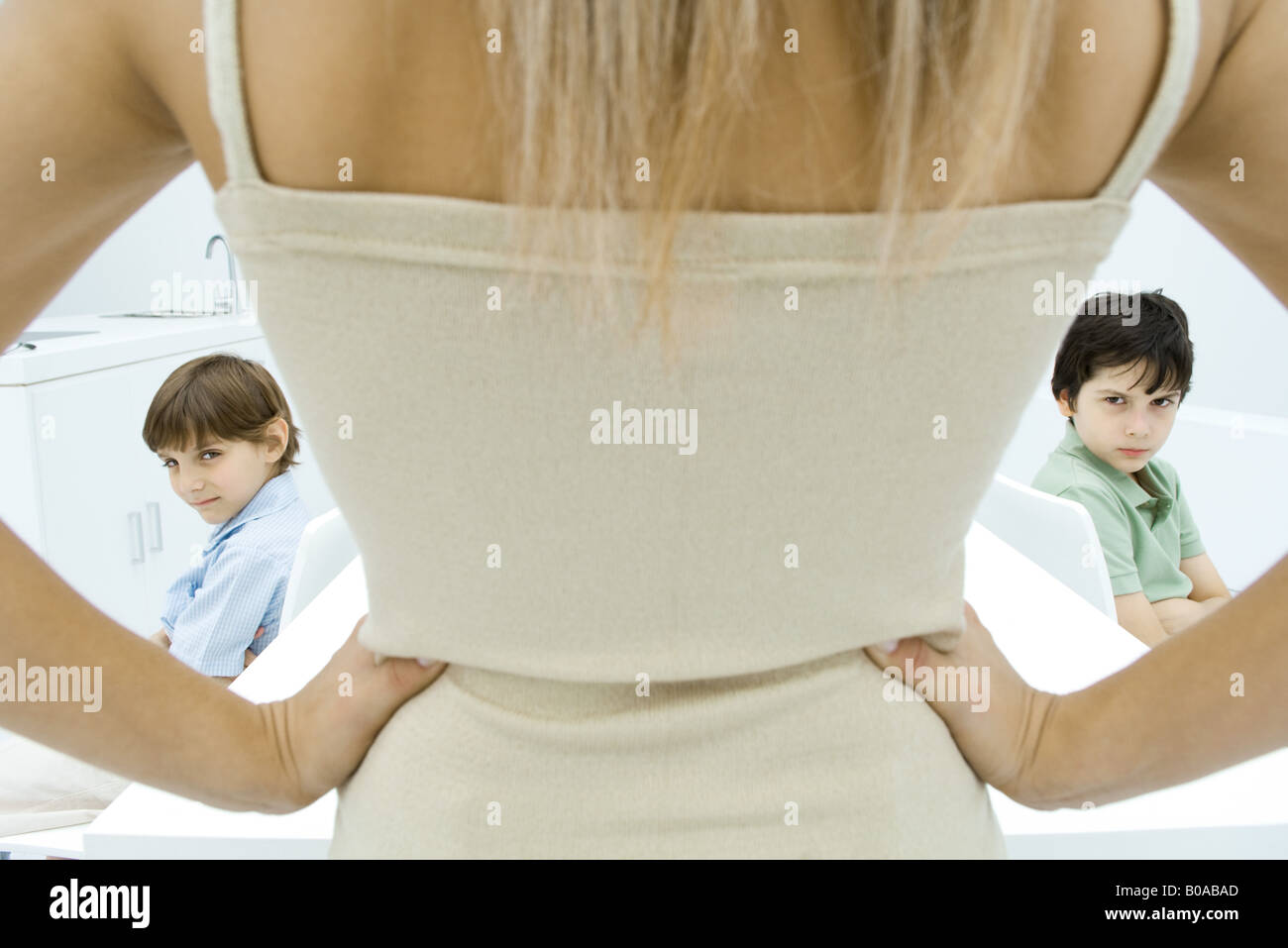Mother standing with hands on hips, rear view, boys sulking in background, cropped view Stock Photo