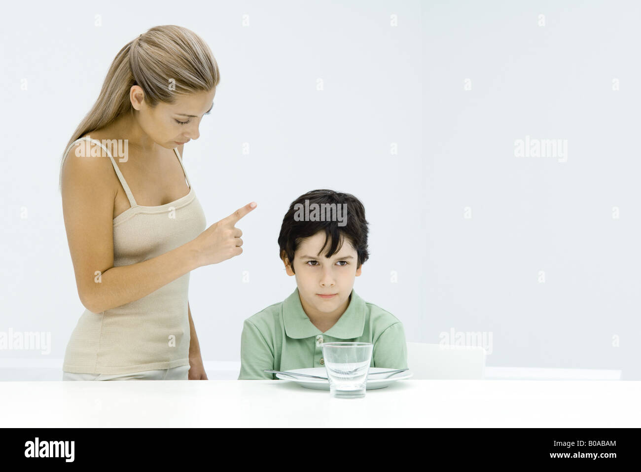 Boy sulking at table, mother standing beside him, shaking her finger Stock Photo