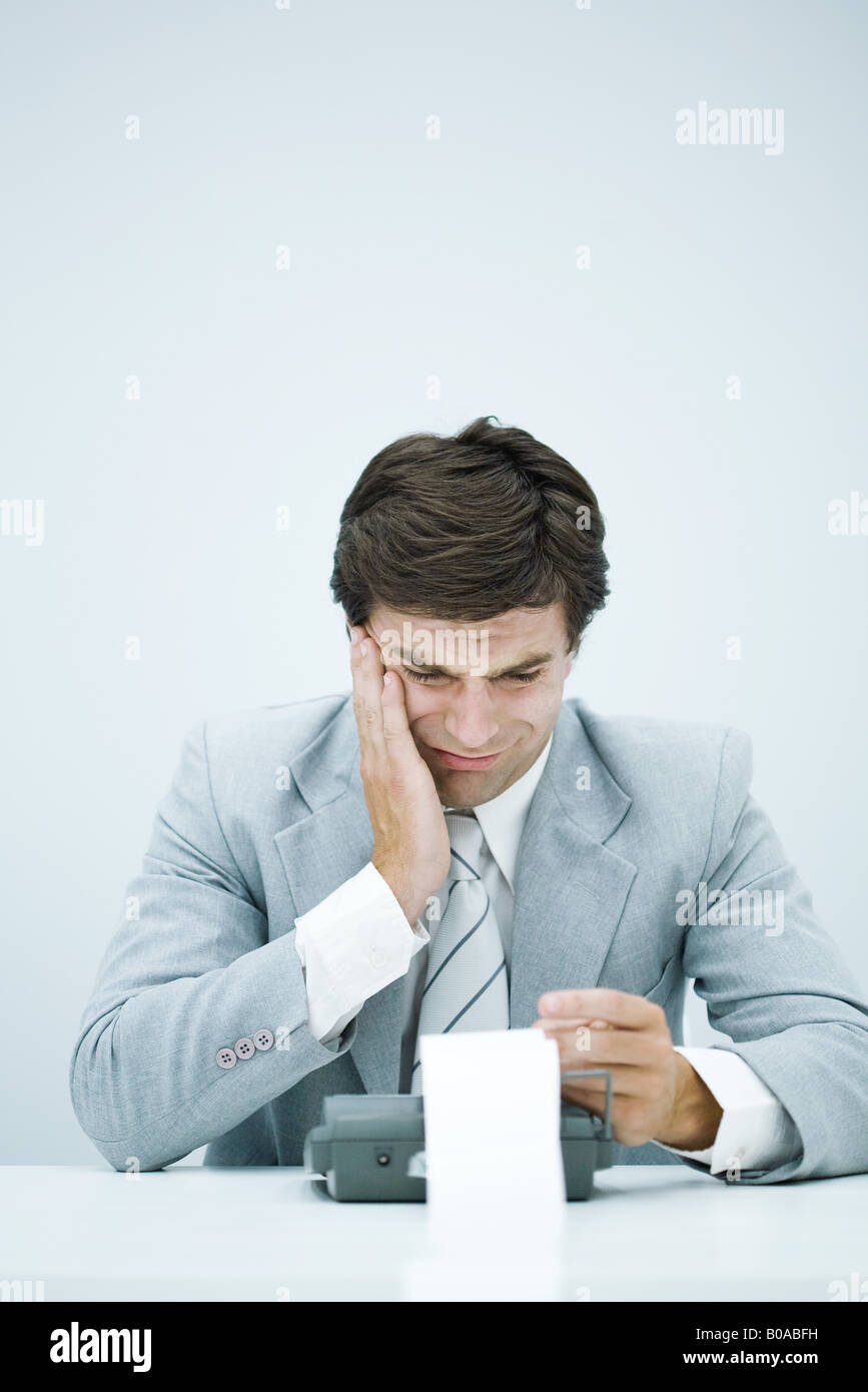 Man in suit looking at printout on calculator, holding head Stock Photo