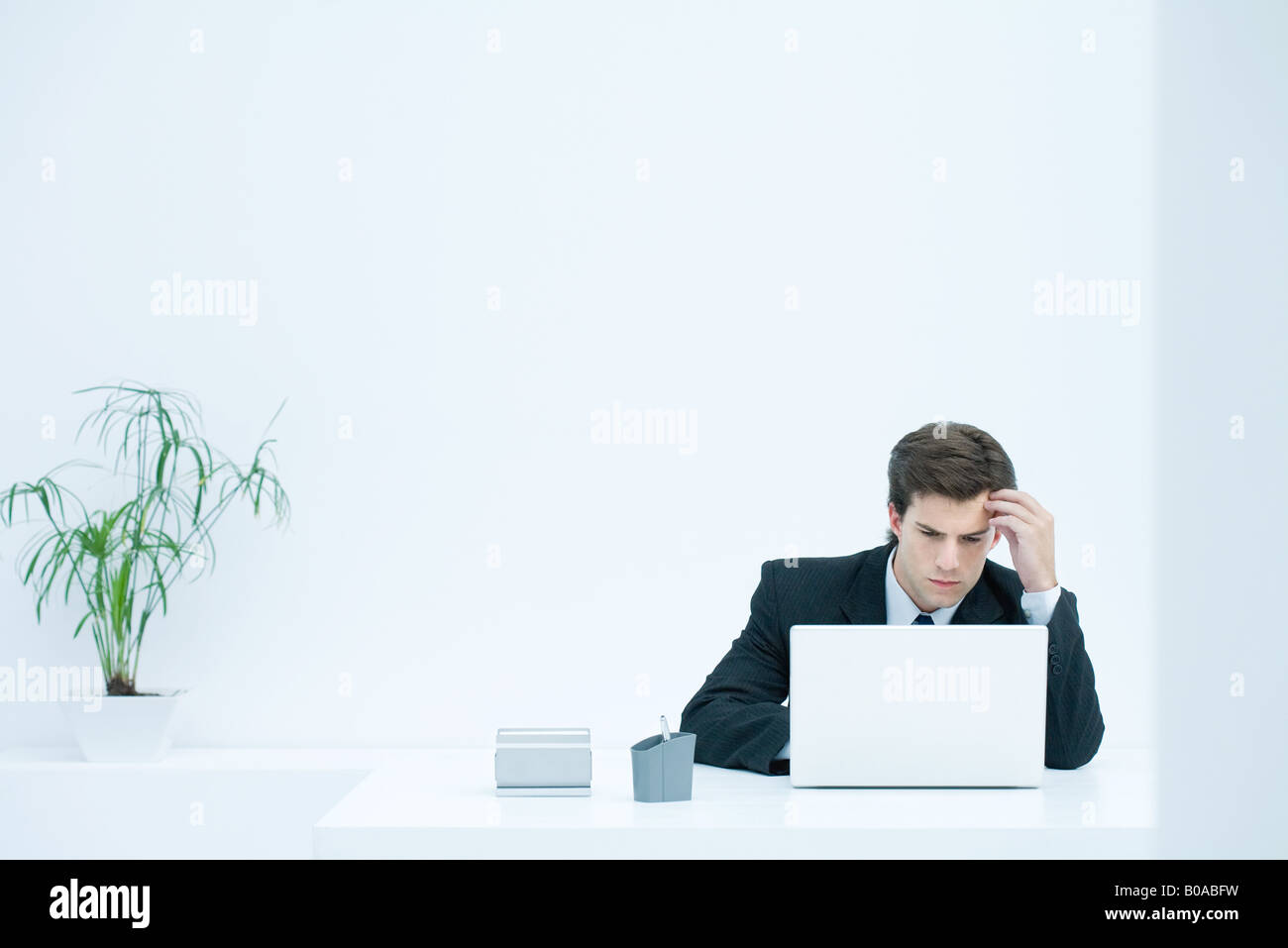 Man sitting at desk, using laptop, holding head Stock Photo - Alamy