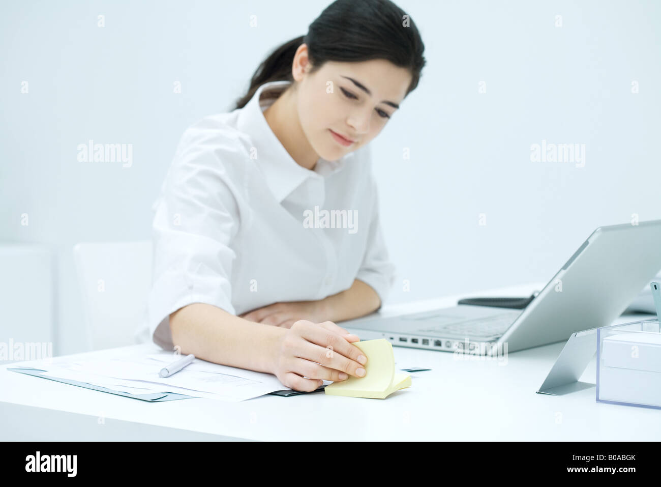 Young woman sitting at desk, flipping through adhesive note block Stock Photo