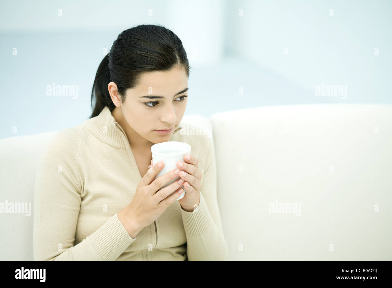 Young woman sitting, holding coffee mug, looking away Stock Photo
