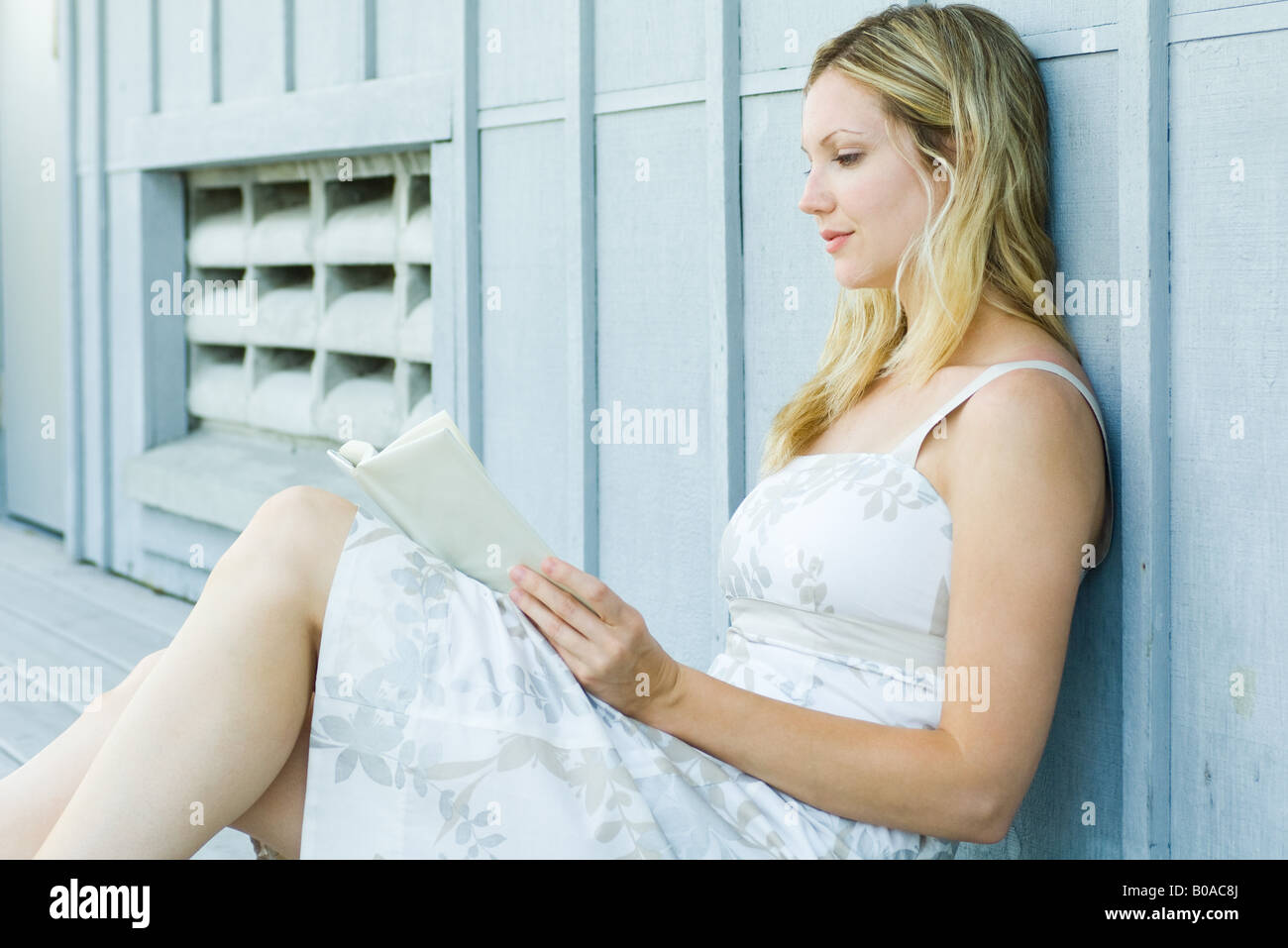 Young woman sitting outdoors, reading book, side view Stock Photo