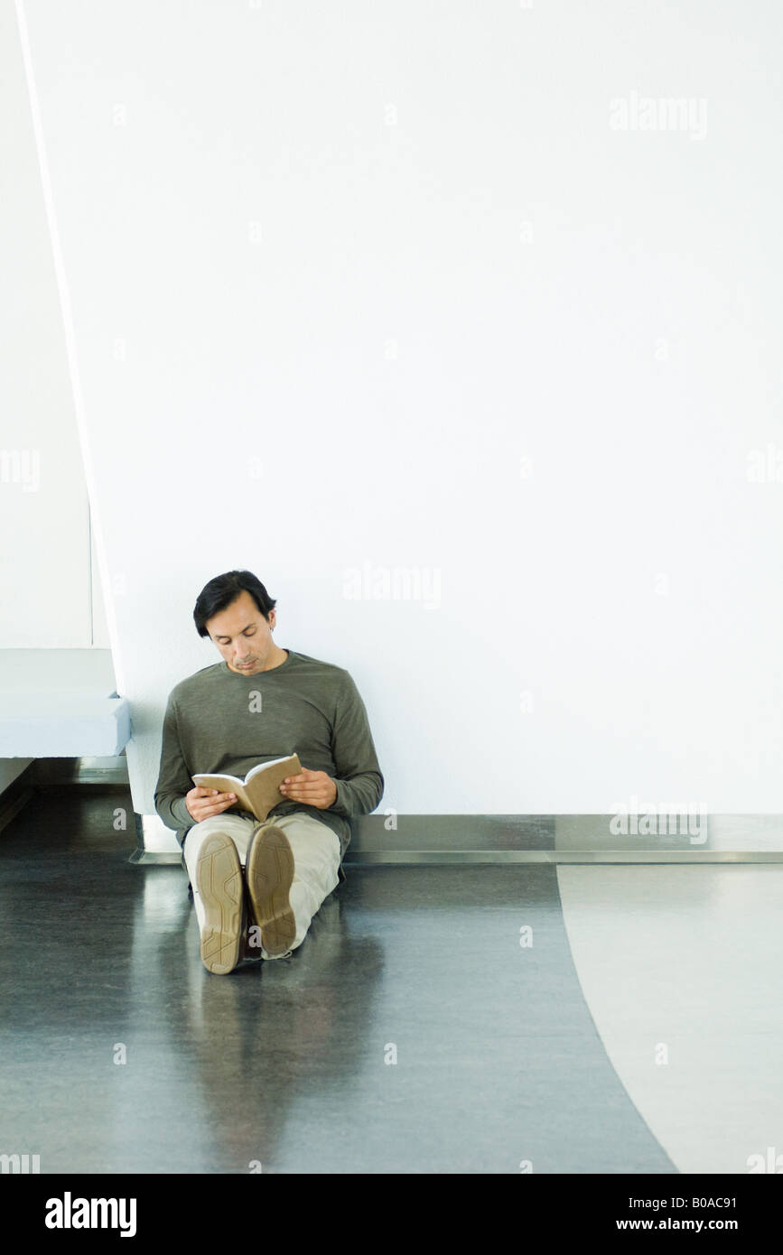 Man sitting on floor, reading book, full length Stock Photo