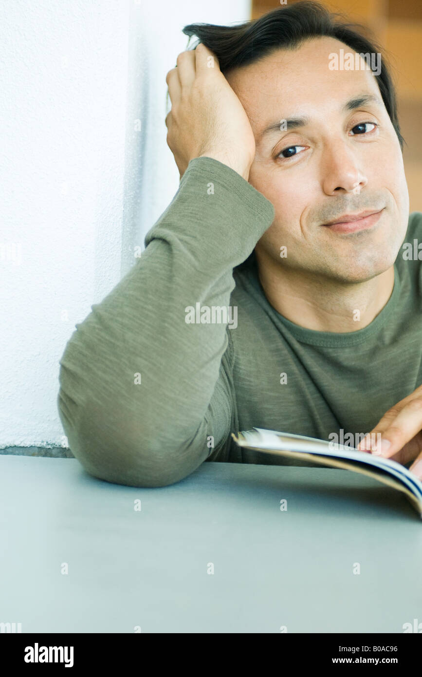 Man with book, holding head, smiling at camera, portrait Stock Photo