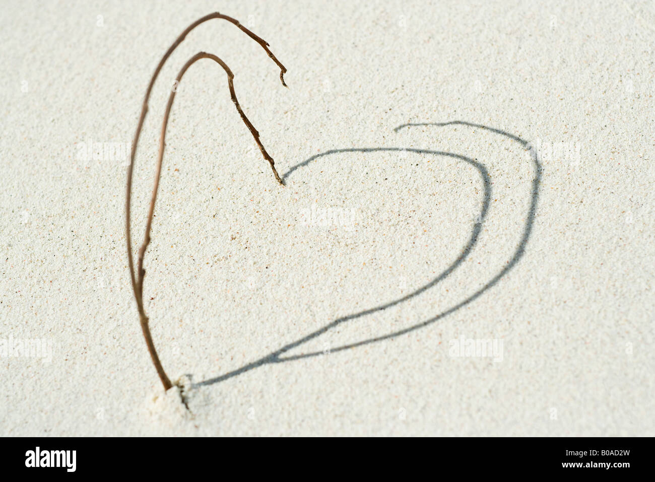 Twigs and shadows arranged in heart shape on the beach, close-up Stock Photo