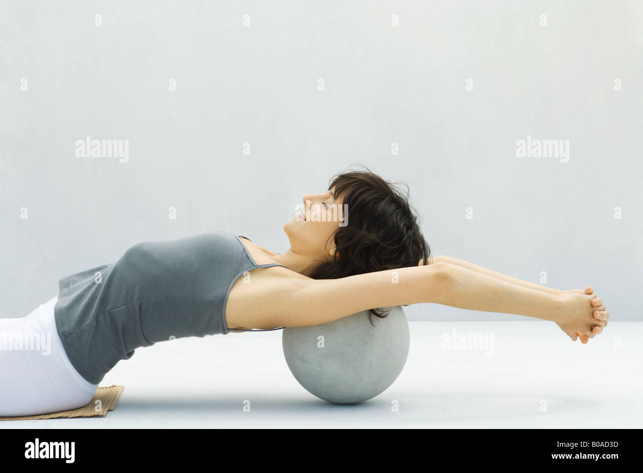 Woman leaning back against fitness ball, arms outstretched, side view Stock Photo