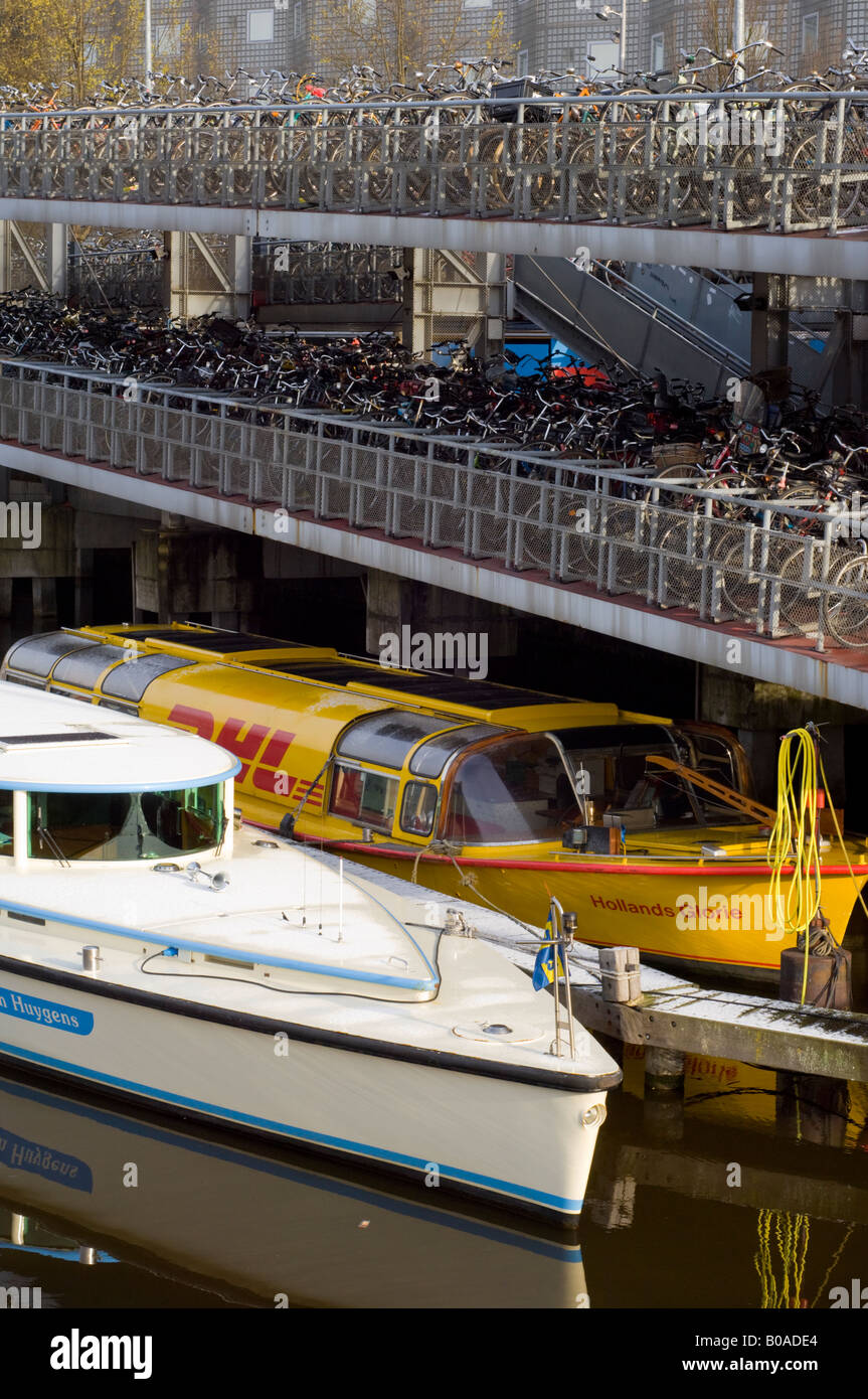 Amsterdam, bicycles parked in a bicycle park at Stationsplein, and two boats moored on Open Haven canal Stock Photo