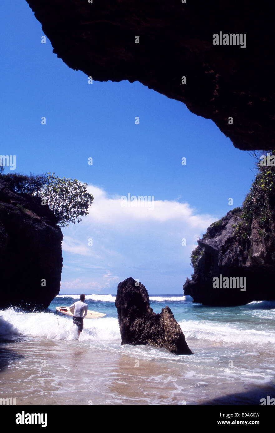 Surfer advances from the caves into the sea at Surfers Retreat Uluwater Bali Indonesia Stock Photo