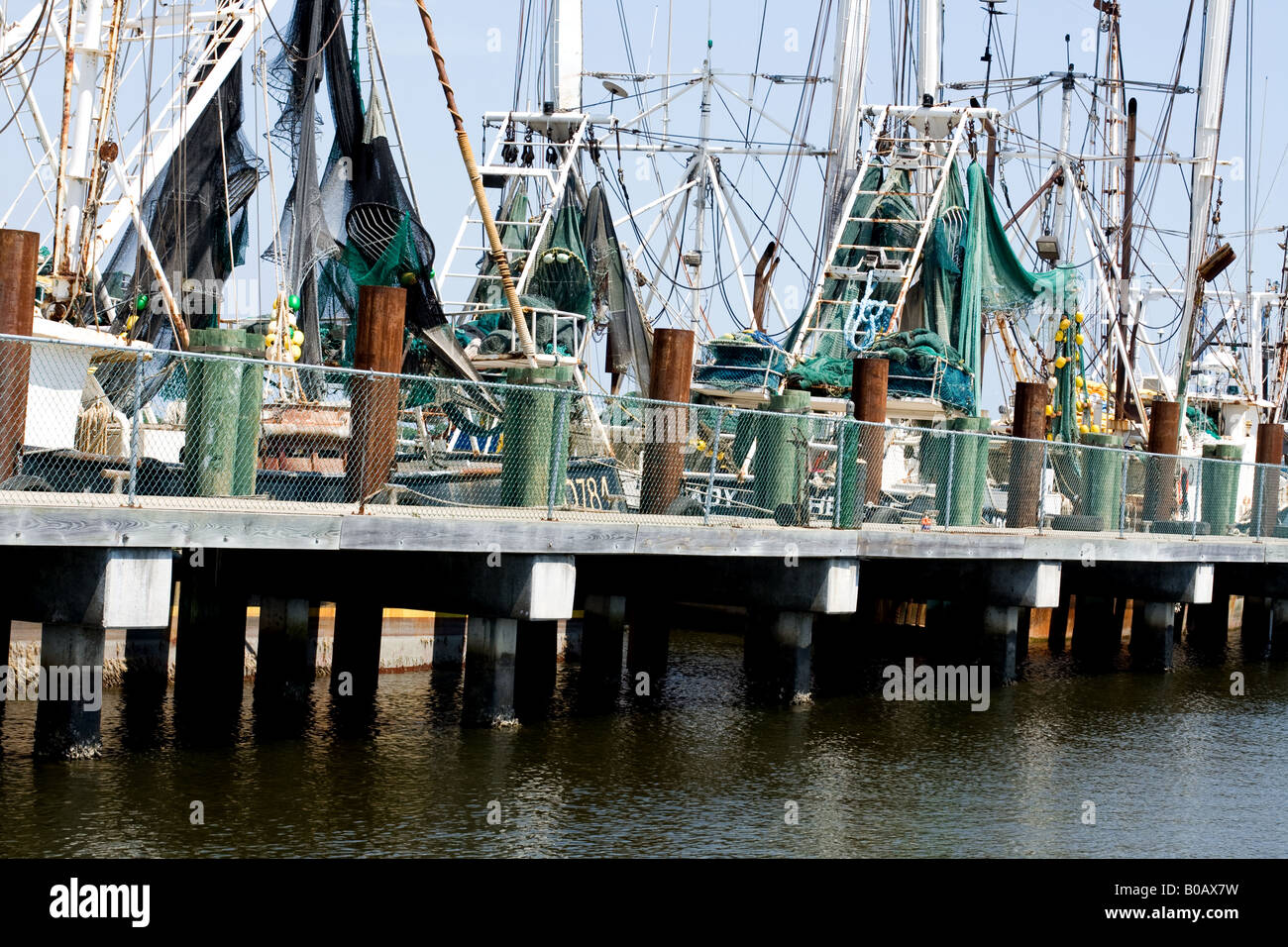 Fishing boats with fishing nets and masts by an elevated dock next to calm water in Mayport, Florida Stock Photo