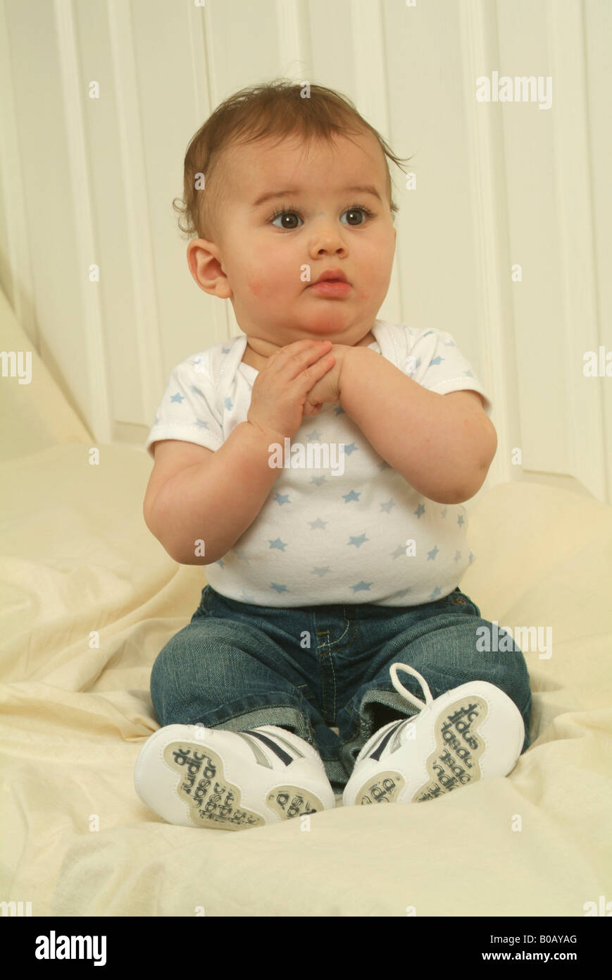 An eight month old baby boy sitting upright on a white couch and