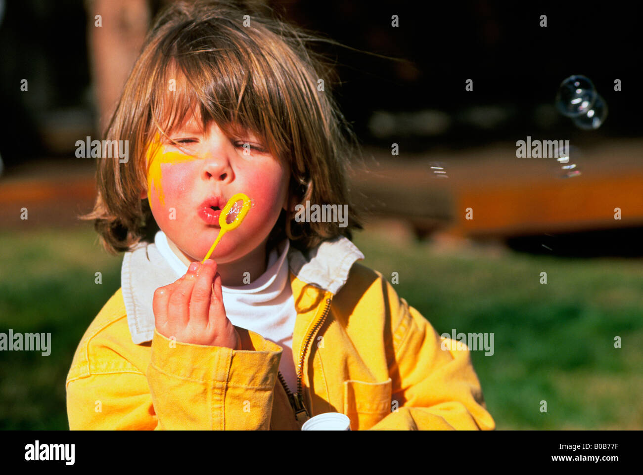 A young girl blows bubbles with a bubble pipe in her front yard Stock