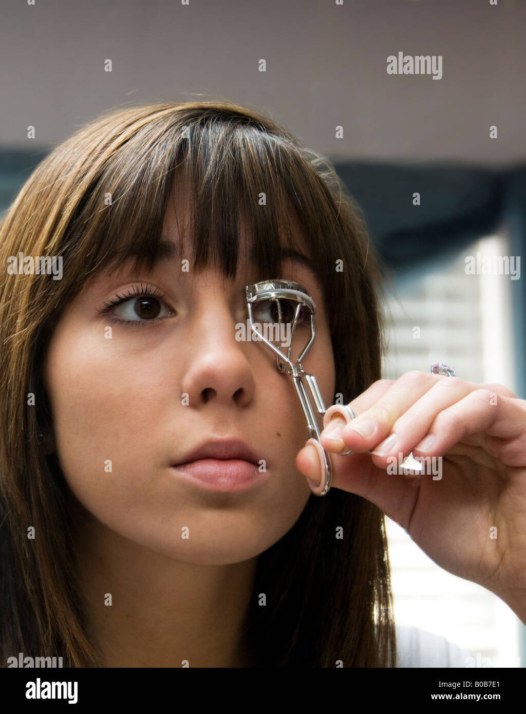 A dark-haired, brown-eyed caucasian fifteen-year-old girl curls her eyelashes. USA. Stock Photo