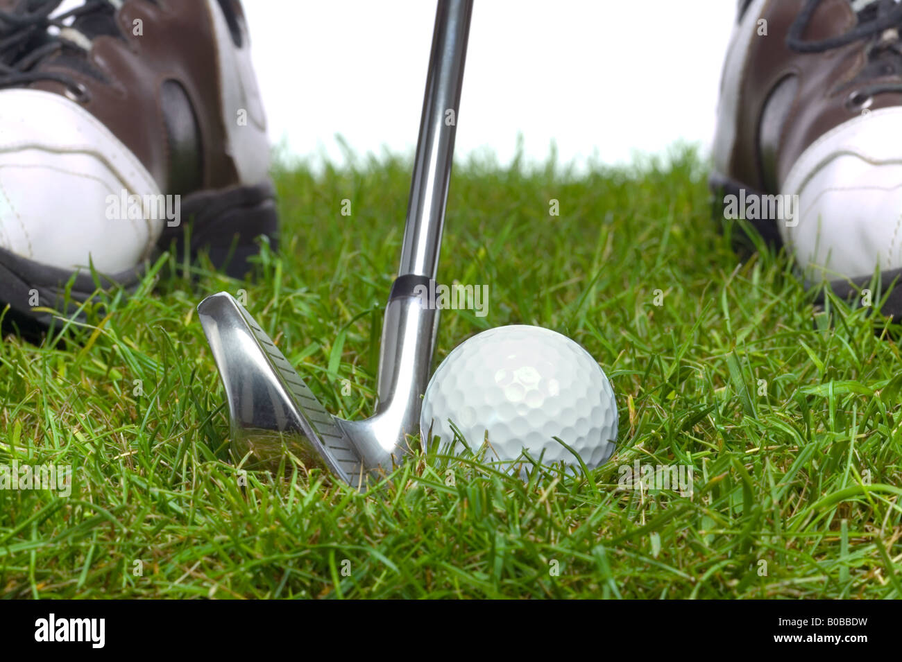 Golf ball in the rough with an iron it behind and the golfers shoes in the background Stock Photo